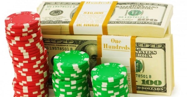 The picture depicts red and green casino bonus chips stacked. The casino bonus chips are in front of a stack of dollar bills.