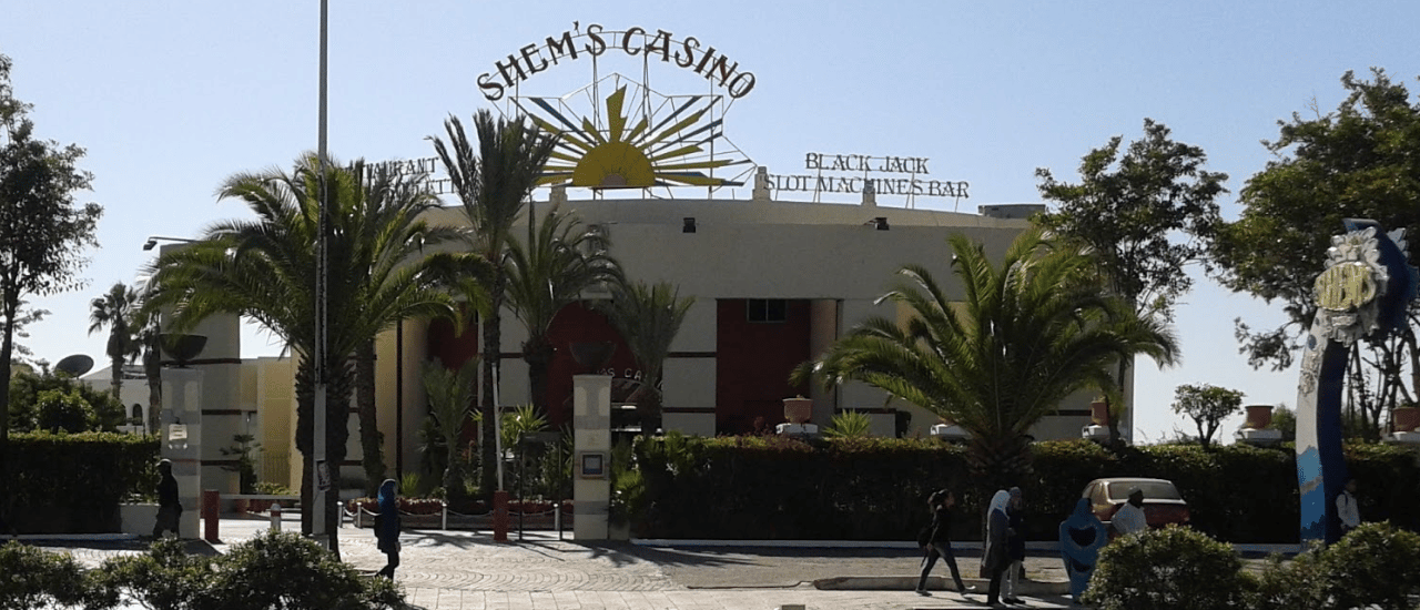 This a photo of the front entrance and logo of Casino Shem's Agadir in the Kingdom of Morocco. Under the picture, on this page, you can read about the legal status of the various forms of Morocco games of chance: internet lottery, digital bingo, electronic poker, sports betting, crypto wagering. There is also info about illegal gambling, betting on blood sports, the licensing system, taxation regime, and you can find a list of licensed online gambling websites, which accept Moroccan players.