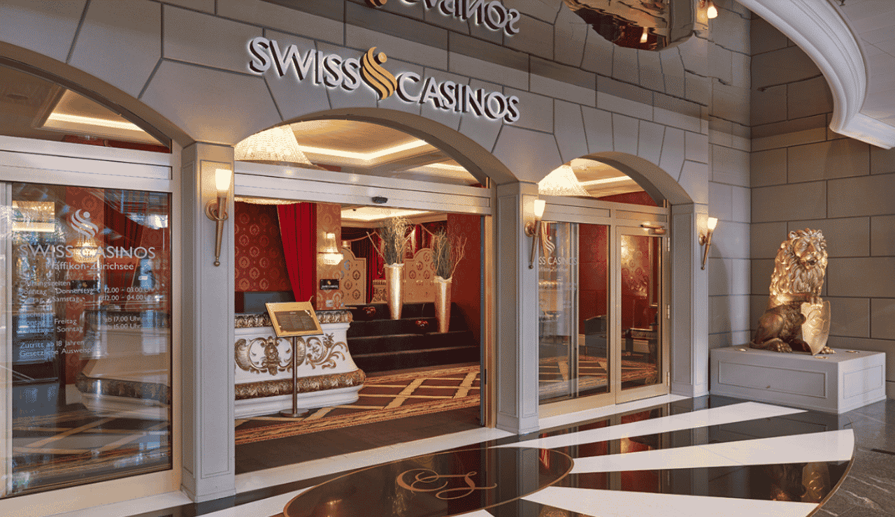 This is a photo of front entrance of the building of Swiss Casinos Pfäffikon, photogrpahed from the outside, from the street, facing the front entrance gate. Casinos Pfäffikon is one of the 4 venues of the company Swiss Casinos (it operates the 4 biggest Switzerland casinos, you can read the details, address, opening hours, dress code, entrance fee, reviews of this venue below, in the casino list). On this page, under the picture, you can find a list of all terrestrial Swiss casinos, and slot halls with review analysis and videos, and you can find a list of licensed online casinos, which accept Switzerland players.
